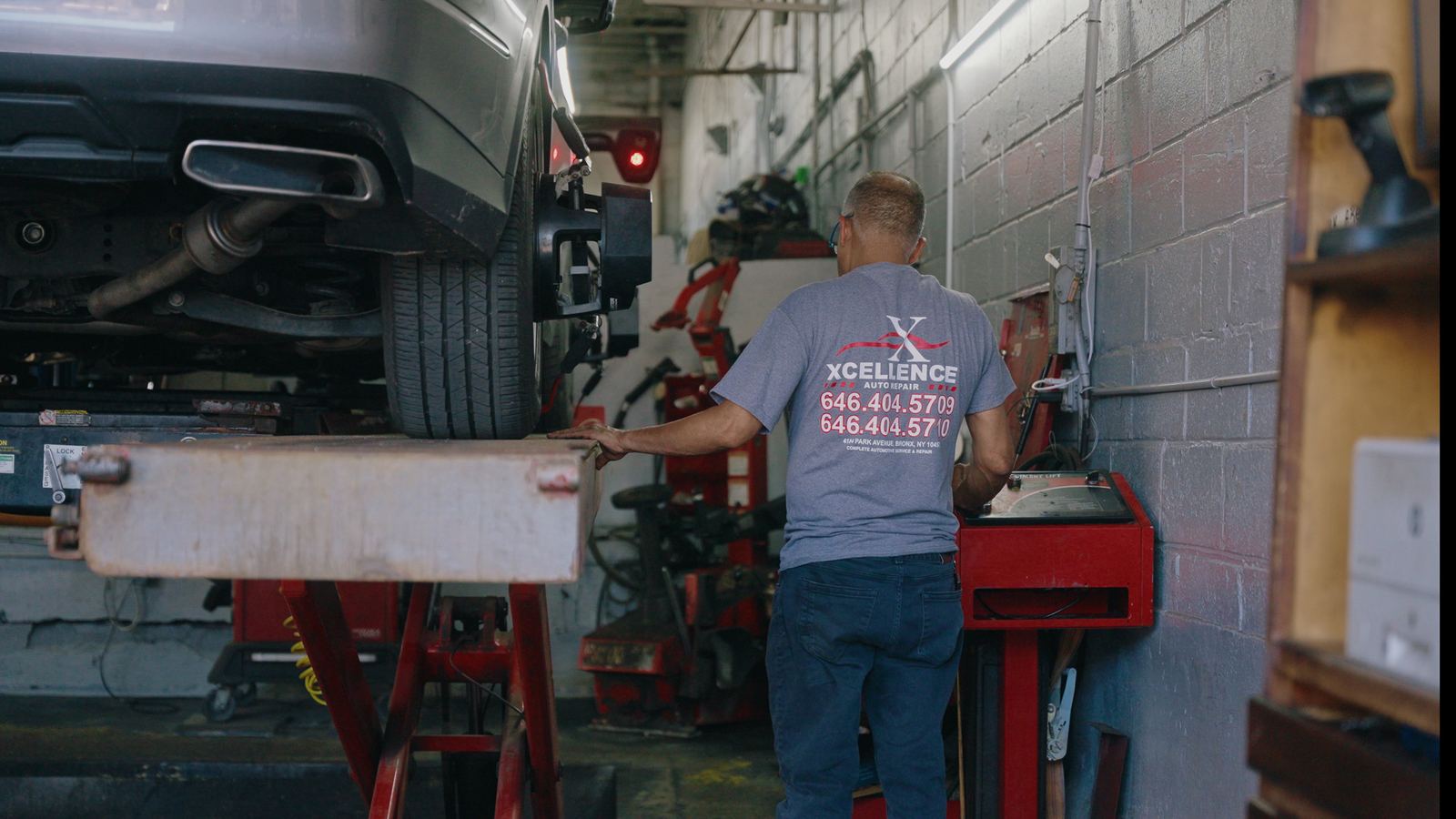 Technician in an Excellence Auto Repair shirt operating the alignment lift